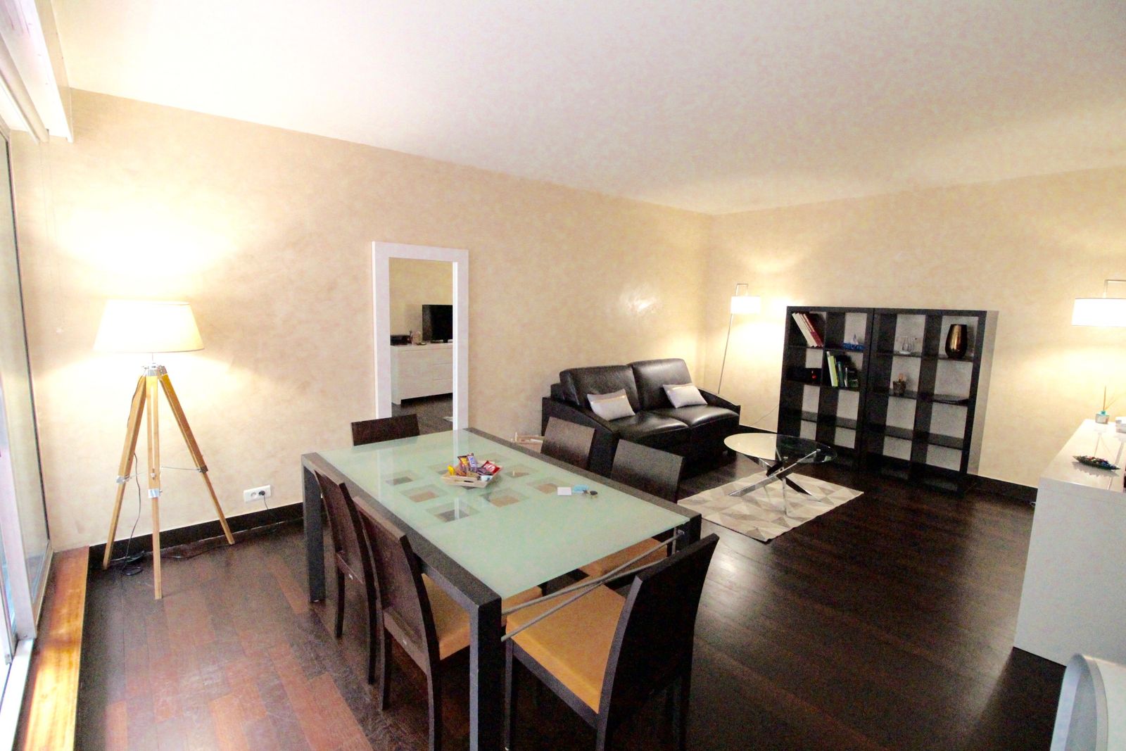 Open-plan living and dining area with glass table, leather sofa, bookcase, and designer lamps